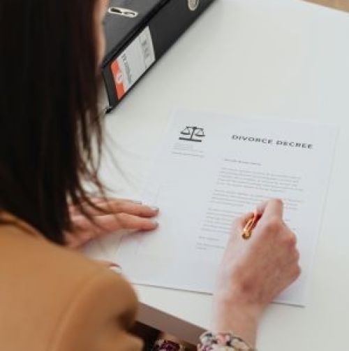 Over the shoulder view of a person signing a divorce decree at a desk in an office.